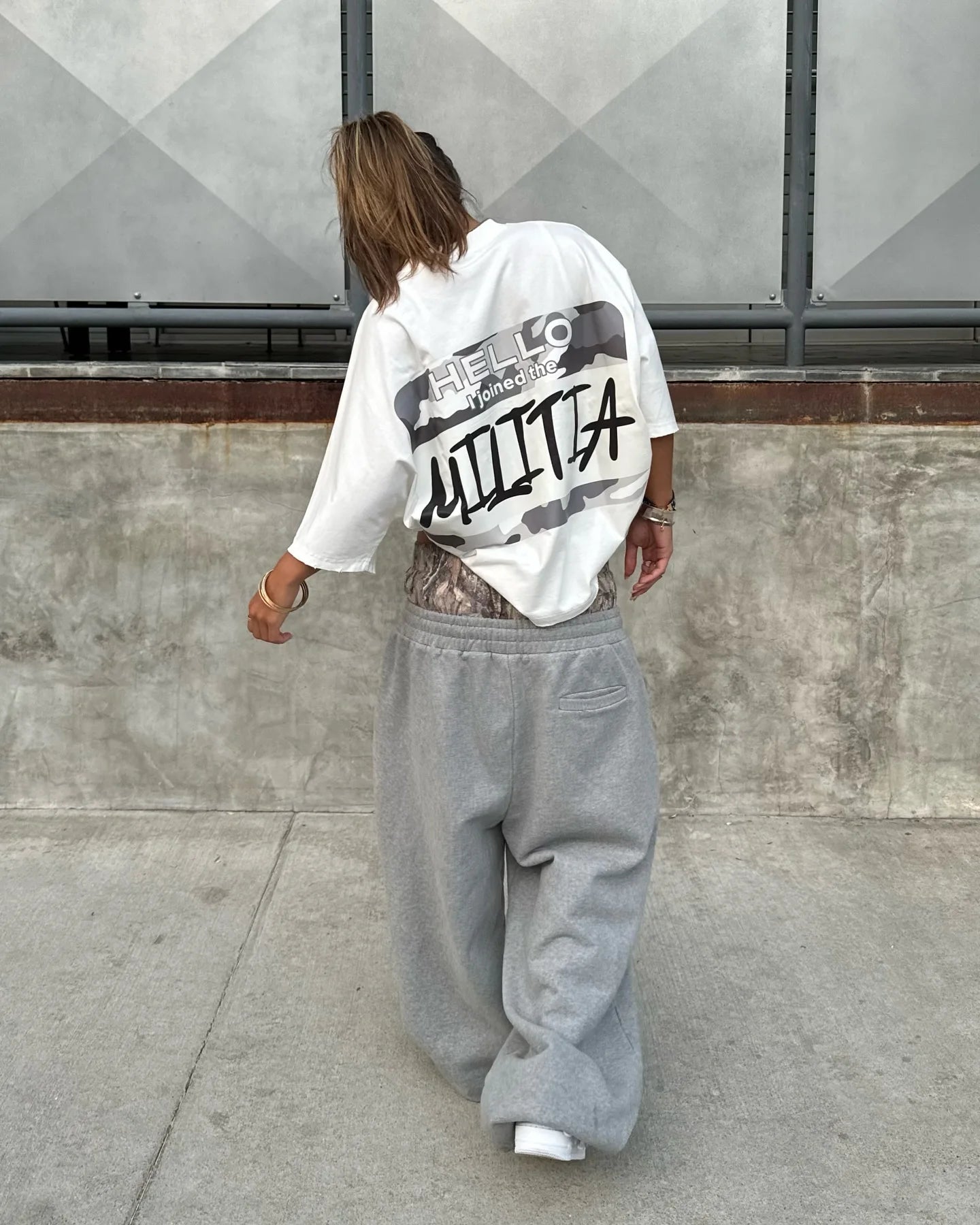 Person wearing a white hoodie with text and gray sweatpants walking on a sidewalk.